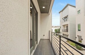 Ein schmaler Balkon mit Metallgeländer, einer Glastür und Blick auf angrenzende Gebäude.