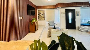 Un soggiorno moderno con parete decorata in legno, una TV a schermo piatto, un tavolino da caffè e un angolo salotto con poltrona e poggiapiedi.