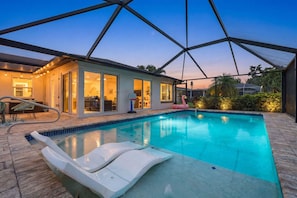 Ein Swimmingpool mit Liegestühlen, eine überdachte Terrasse und ein Haus mit großen Fenstern.