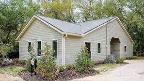 A single-story building with a gabled roof, a covered porch, and a small attached garage. - Superior Queen Two-Bedroom Cottage - no pets (Bronson)