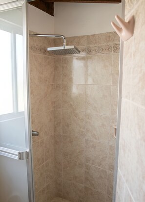 Een badkamer met beige tegels, een douche met handdouche en een deur met metalen handvat.