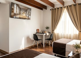 Una habitación con una cama, un escritorio, dos sillas, un ventanal con cortinas y un cuadro en la pared.