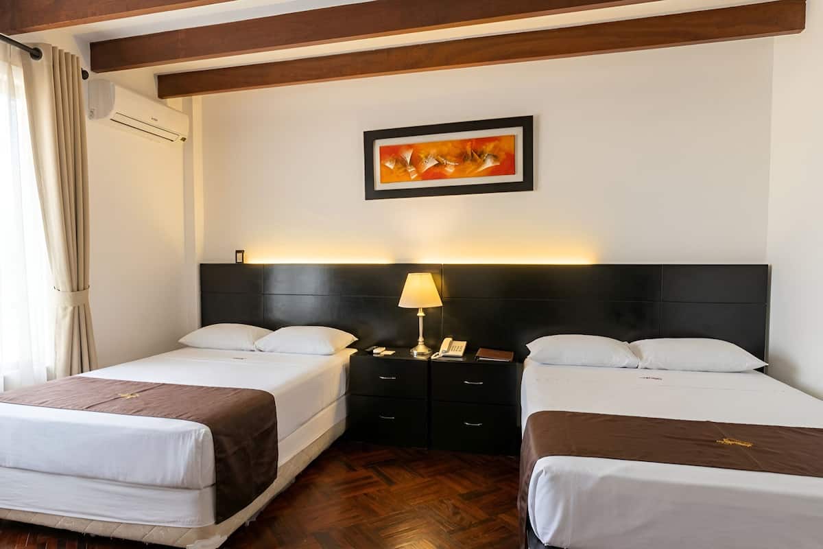 A hotel room with two beds, a nightstand with a lamp, a framed picture on the wall, and wooden beams on the ceiling.