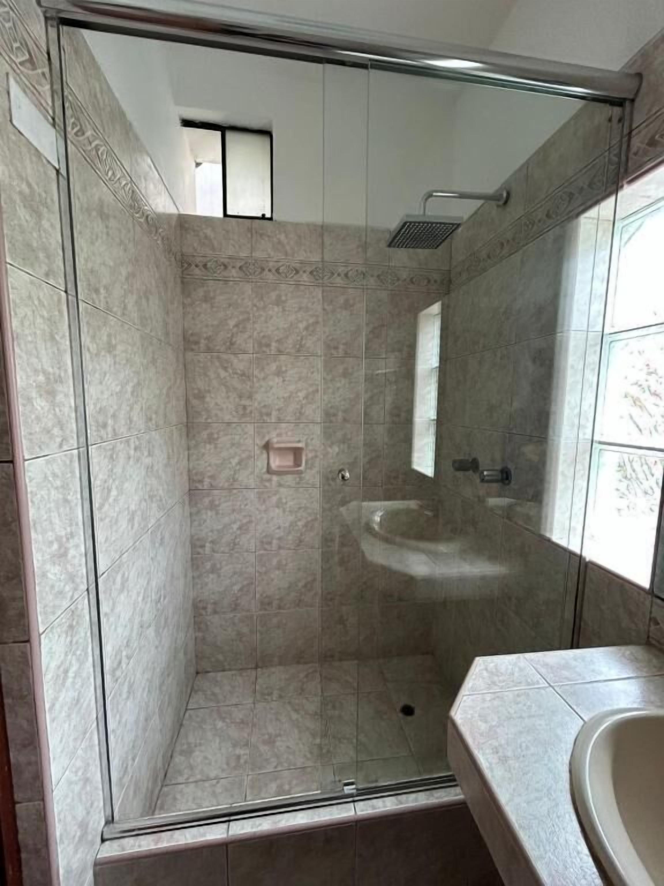 Eine Dusche mit Glastür, ein Waschbecken und ein Spiegel.