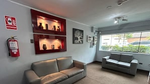 Un vestíbulo con un sofá gris, otro sofá gris, un extintor rojo y una estantería de pared con objetos decorativos.