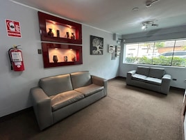 Un vestíbulo con un sofá gris, otro sofá gris, un extintor rojo y una estantería de pared con objetos decorativos.