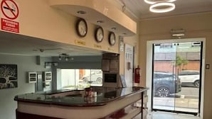 Un mostrador de recepción con un reloj, un cartel de prohibido fumar y una puerta de vidrio que da al exterior.