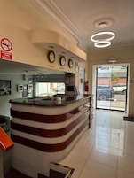 Un mostrador de recepción con un reloj, un cartel de prohibido fumar y una puerta de vidrio que da al exterior.