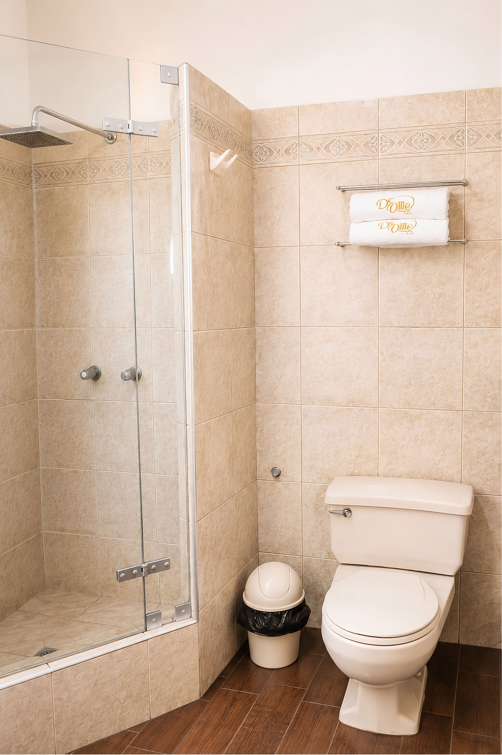 A bathroom with a glass-enclosed shower, a toilet, and a trash bin.