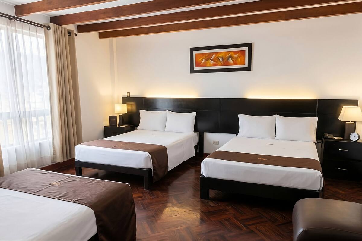 A hotel room with two beds, a desk, a chair, a painting on the wall, and a window with curtains.