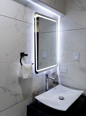 Ein Badezimmer mit einem weißen Waschbecken, einem Spiegel mit LED-Beleuchtung, einem Handtuchhalter und Marmorwänden.