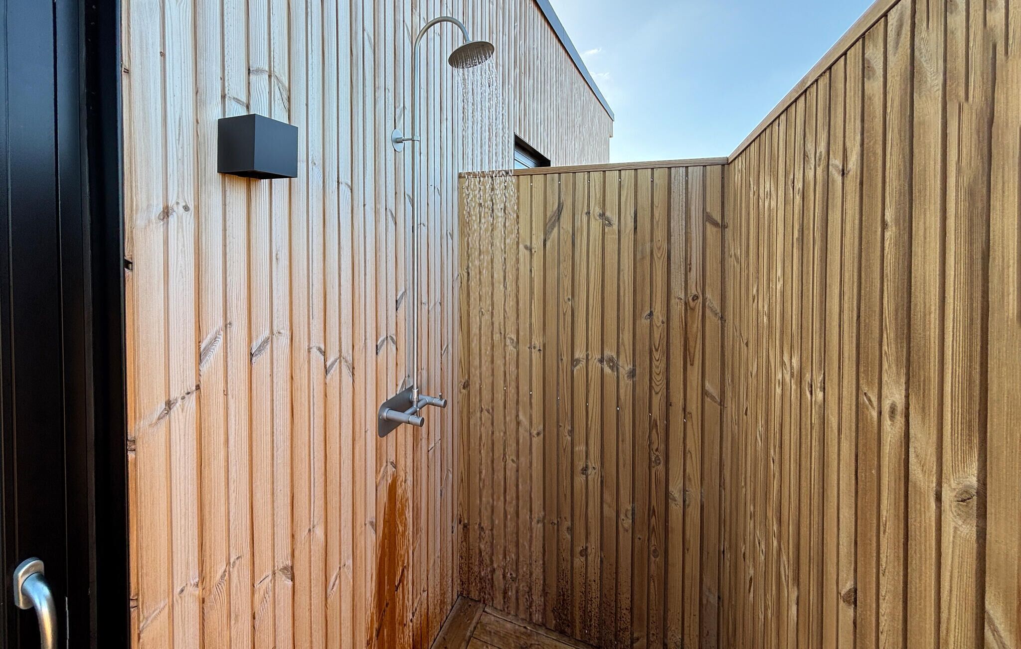 A wooden fence with a metal gate, a black door, and a showerhead.