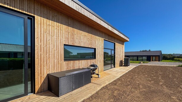 A modern building with large windows, a wooden exterior, and a patio area with outdoor furniture. - Gorgeous home in Haderslev with sauna (Haderslev)
