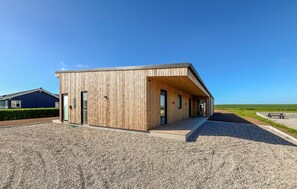 Ein modernes Holzgebäude mit geneigtem Dach, einer Schotterauffahrt und einer Bank im Hintergrund.