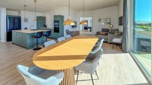 A modern kitchen with a central island, a dining area with a large wooden table, and a living room with a sofa and a TV. - Gorgeous home in Haderslev with sauna (Haderslev)