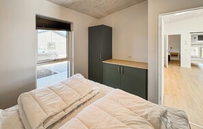 Ein Schlafzimmer mit einem Bett, einem Fenster mit Jalousien, einem dunklen Schrank und Holzboden.