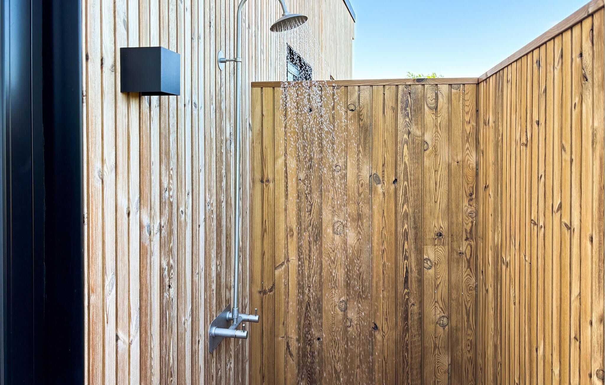 Una valla de madera con una reja metálica, un aplique de pared y un tubo de metal.
