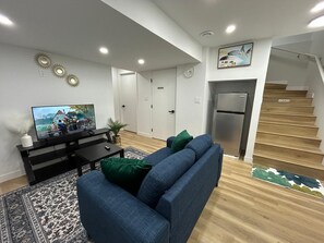 A modern living room with a flat-screen TV, a sofa, a coffee table, and a staircase leading to an upper level.