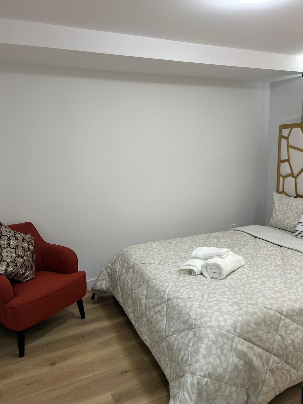 Un dormitorio con cama, un sillón rojo y un elemento decorativo en la pared.