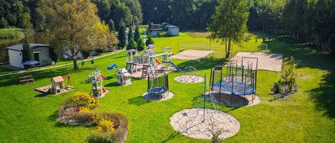 An aerial view of a park with playground equipment, a small house, and a pond.