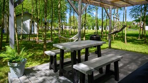 A covered outdoor area with a picnic table and benches, surrounded by trees and a grassy field. - Comfortable Holiday Home no. 1B With a Fireplace (Darlowo)