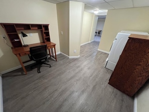 Ein Zimmer mit einem Holztisch, einem schwarzen Bürostuhl und einem weißen Kühlschrank.