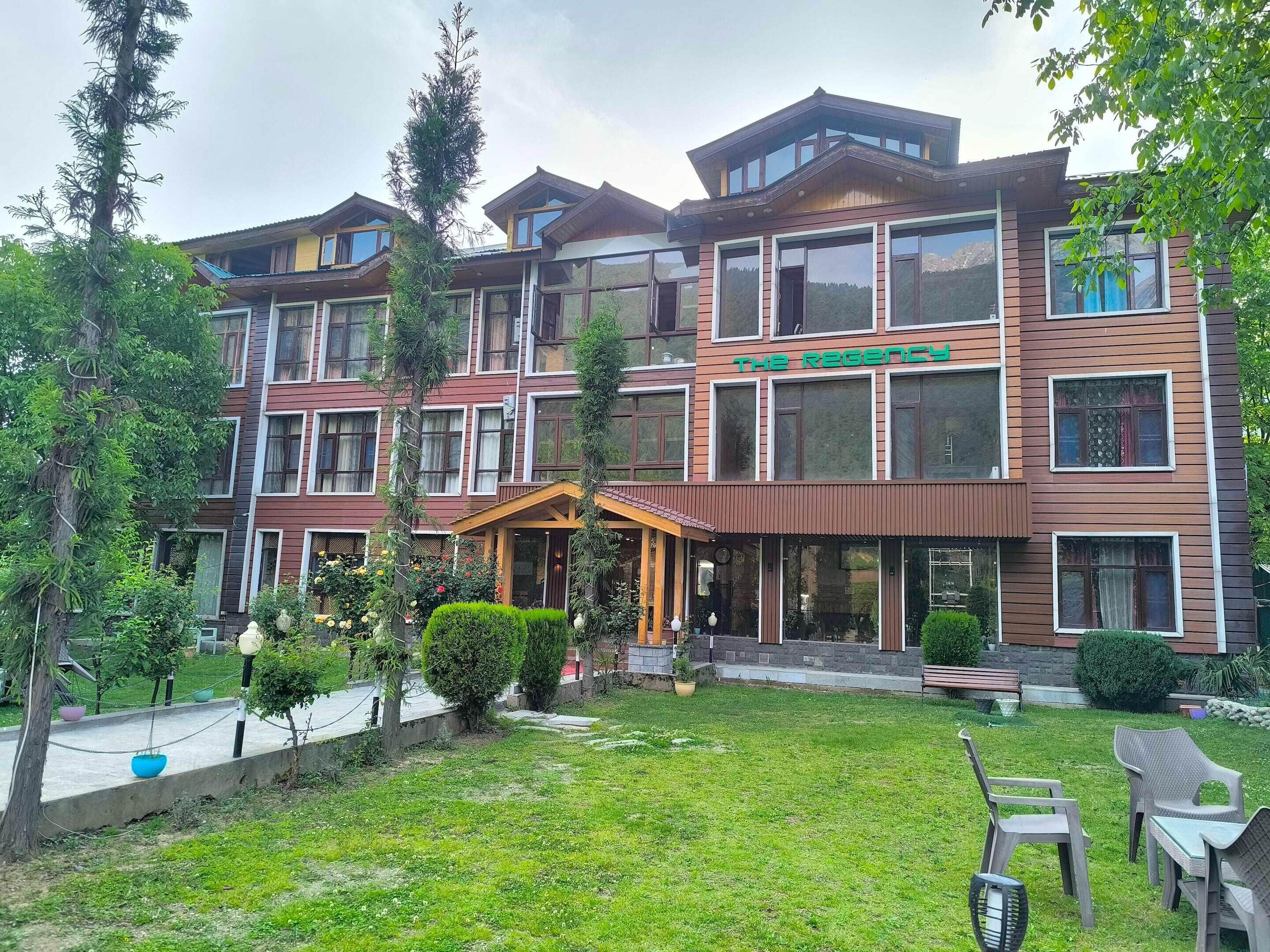 A multi-story hotel with a central entrance, a well-maintained lawn, and outdoor seating.