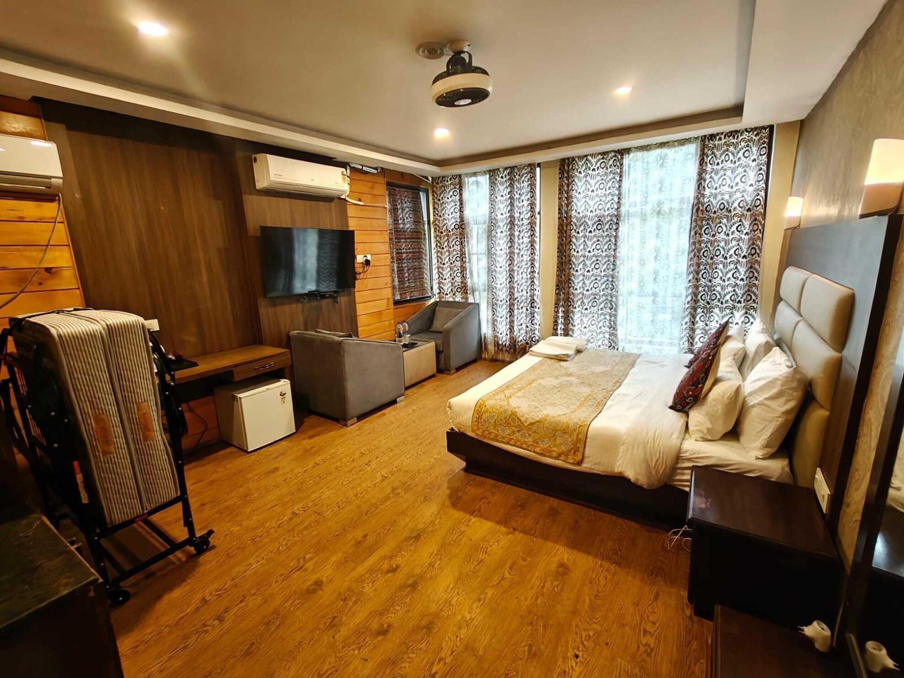 A hotel room with a bed, a desk, a chair, a TV, and an air conditioning unit.