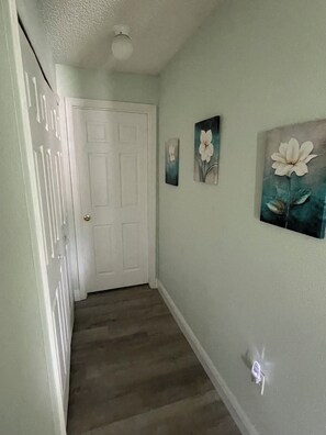 Ein Korridor mit einer weißen Tür, einem Lichtschalter und drei an der Wand befestigten Bildern von Blumen.