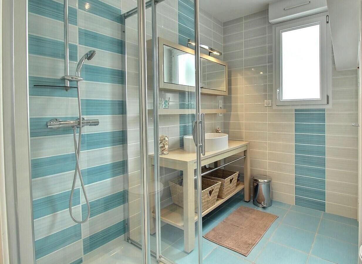 Een badkamer met een douchecabine van glas, een wastafel, een spiegel en een raam.