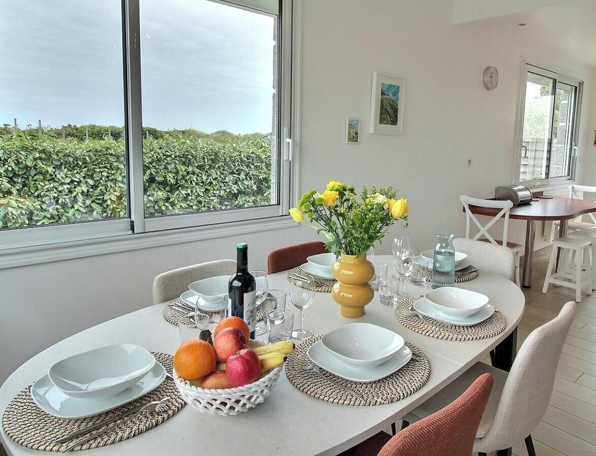 Een eethoek met een tafel voor vier personen, een fruitmand, een vaas met bloemen en een fles wijn.