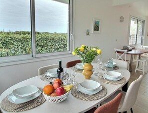 Ein Essbereich mit einem Tisch für vier Personen, einem Obstkorb, einer Blumenvase und einer Weinflasche.