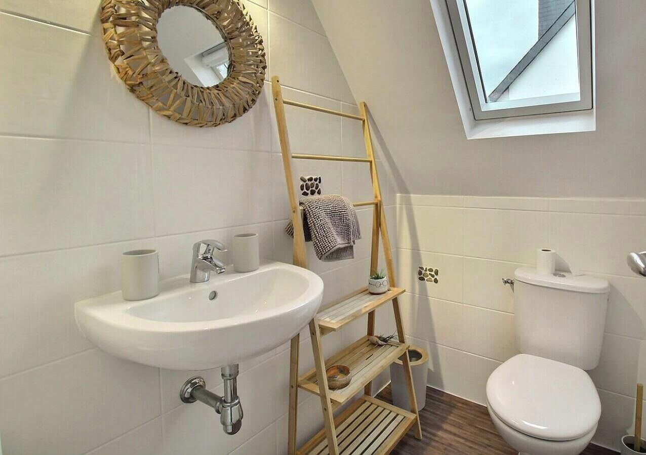 A bathroom with a white sink, toilet, and wooden ladder shelf.