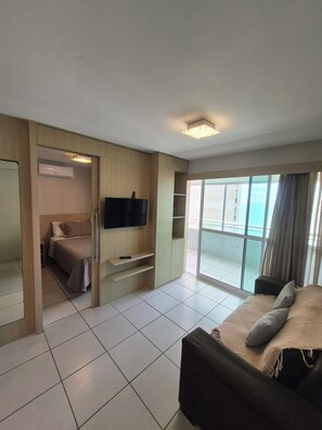 Ein Hotelzimmer mit Bett, Fernseher, Balkon mit Blick und einer Schiebetür zu einem weiteren Raum.
