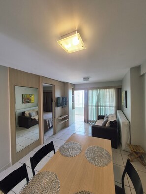 Ein modernes Wohnzimmer mit Essbereich, einem an der Wand montierten Fernseher und einem Balkon mit Vorhängen.