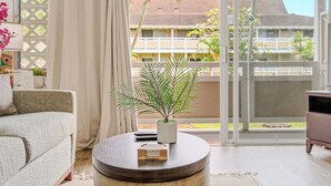 Ein Wohnzimmer mit einer Couch, einem runden Couchtisch mit einer Pflanze, einer Fernbedienung und einer kleinen Holzschale.