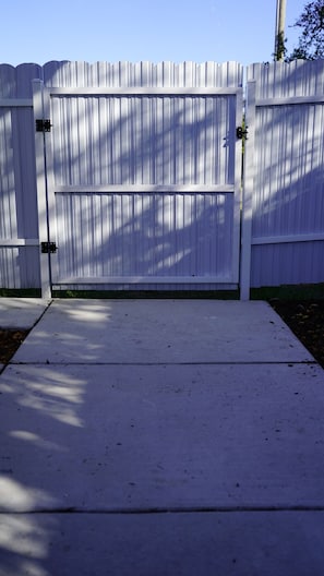 A white metal gate with a concrete driveway leading to a fenced area.