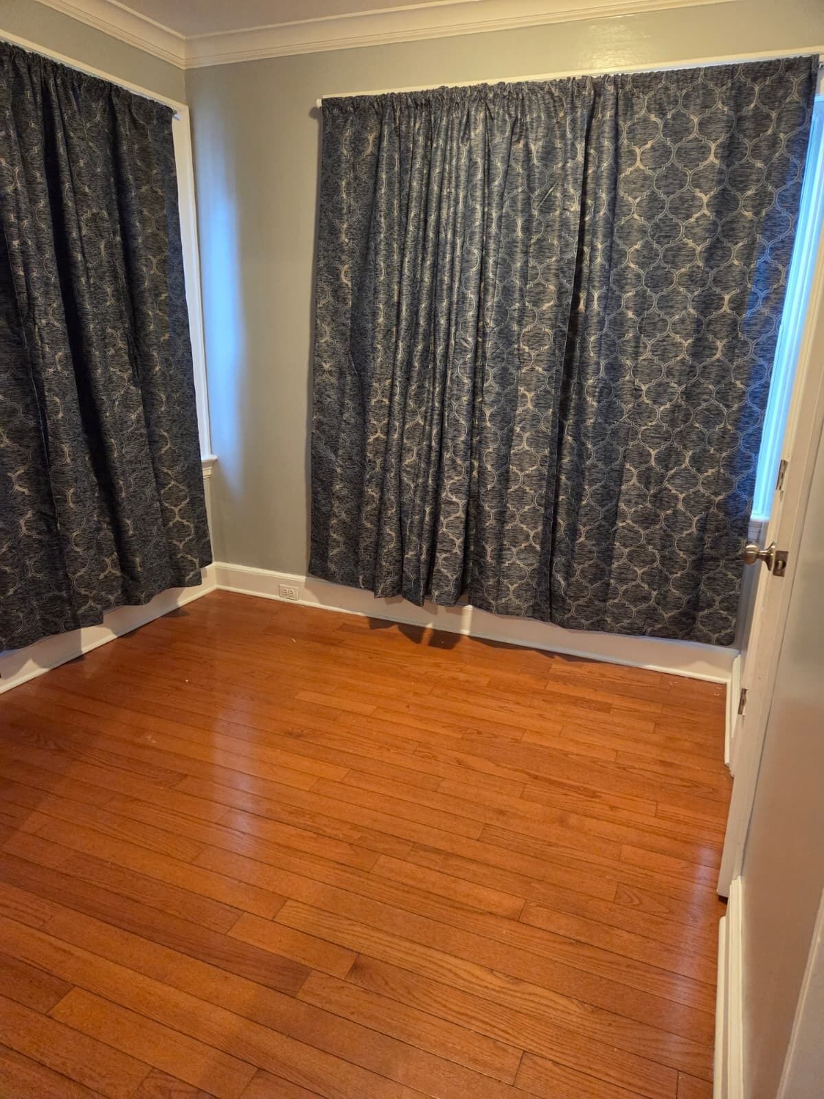 A room with wooden flooring, a window with a view, and patterned curtains.