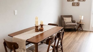 Un'area pranzo con un tavolo in legno e sedie, un tavolino laterale con una lampada e una poltrona grigia.