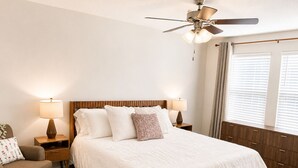 Una camera da letto con un letto, due comodini, una sedia, una ventola a soffitto e una finestra con persiane.