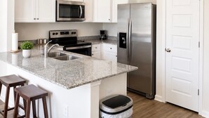 Una cucina moderna con mobili bianchi, elettrodomestici in acciaio inossidabile, un piano di lavoro in granito e un cestino.