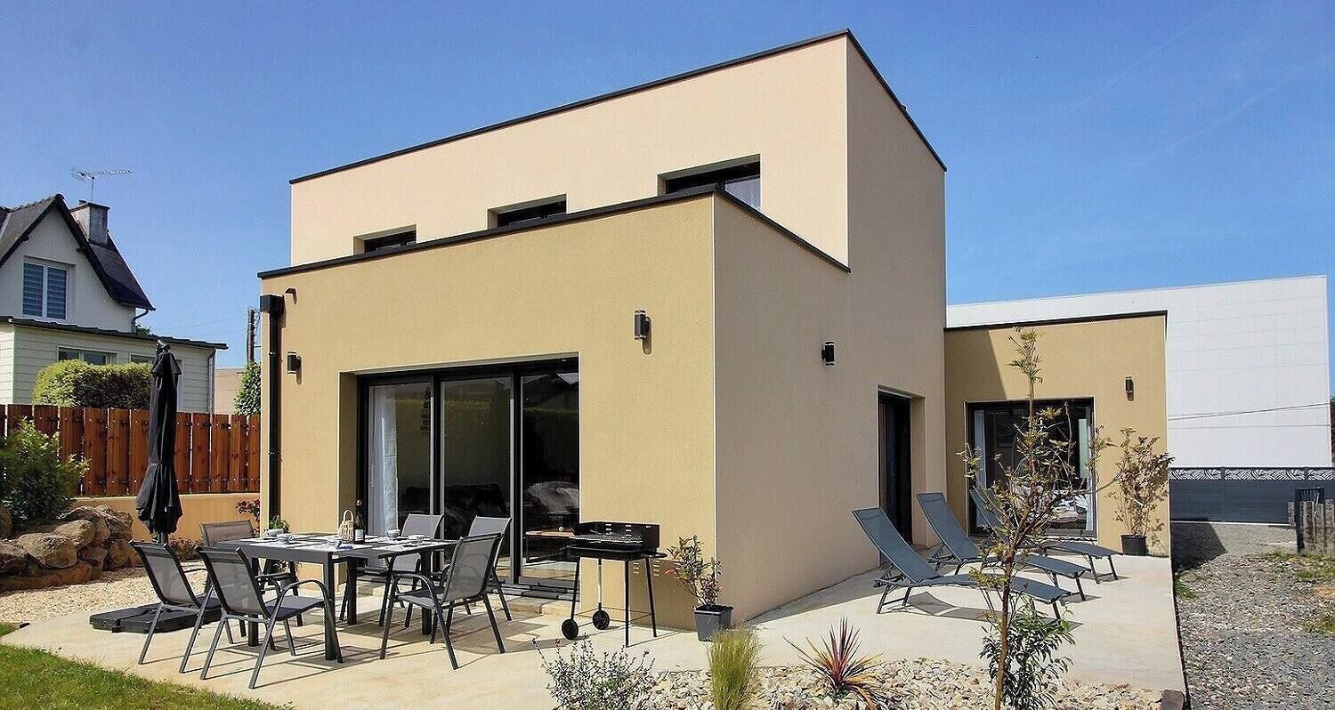 Ein modernes, zweistöckiges Haus mit einer Terrassenfläche, ausgestattet mit Tisch, Stühlen, einem Grill und Liegestühlen.