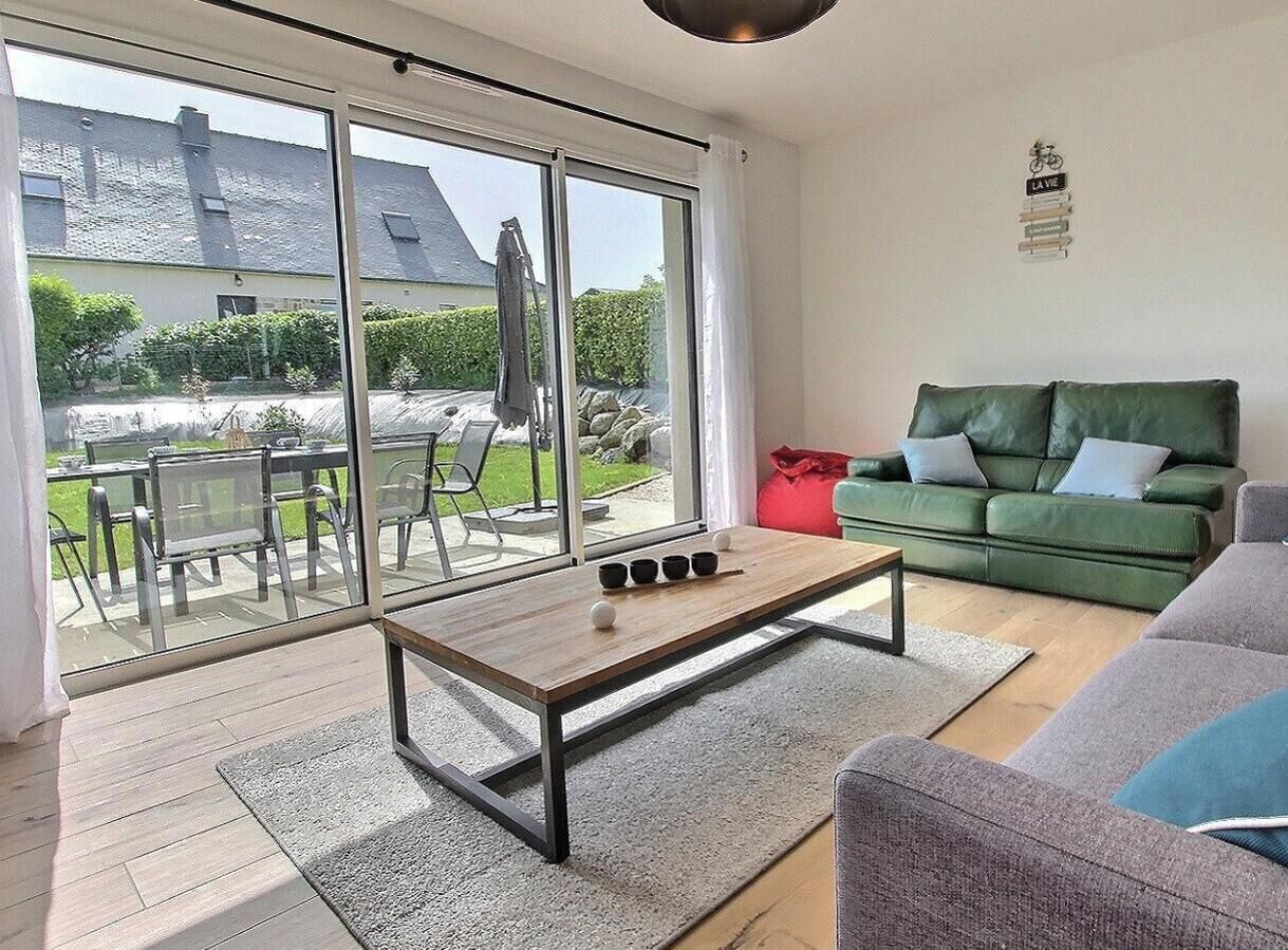 Un salon moderne avec une porte vitrée donnant sur une terrasse extérieure, un canapé vert et une table basse en bois.