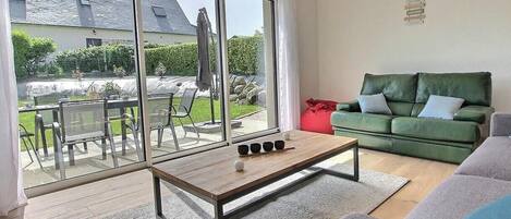 Una sala de estar moderna con un ventanal de vidrio que da a un patio exterior, un sofá verde y una mesa de centro de madera.