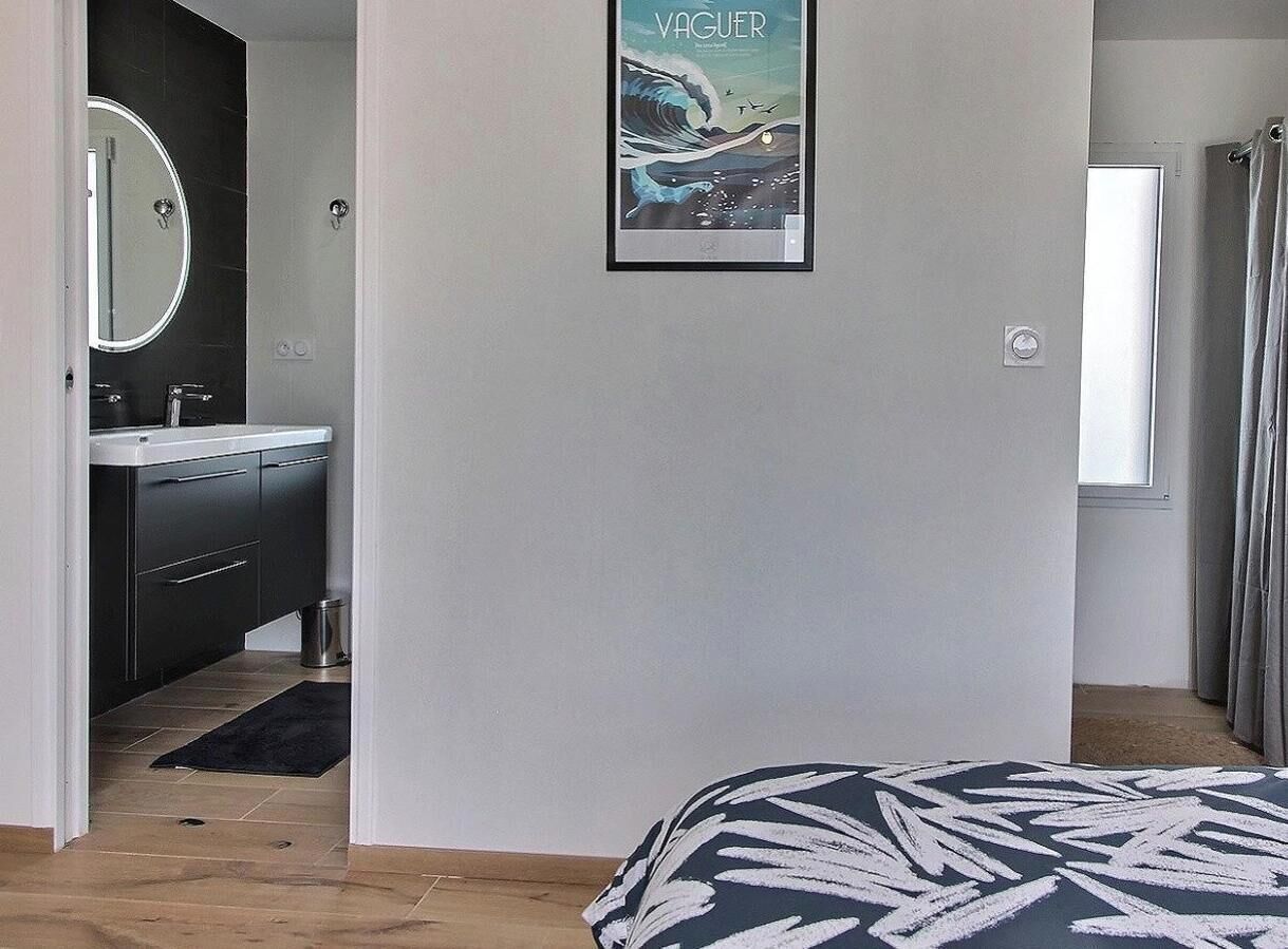 Una camera da letto con un letto, un bagno con uno specchio e un lavandino, e un quadro appeso al muro.