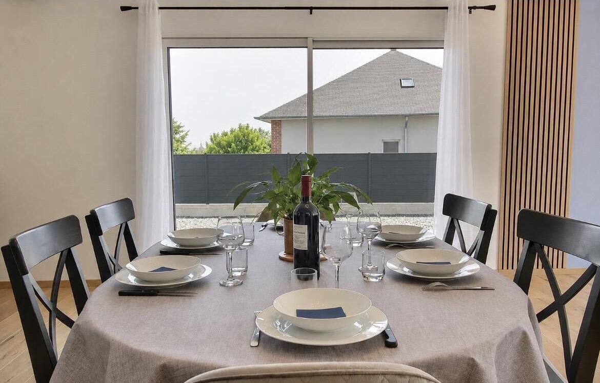 Mesa de comedor lista para cuatro personas, con sillas, una planta en maceta y copas de vino.