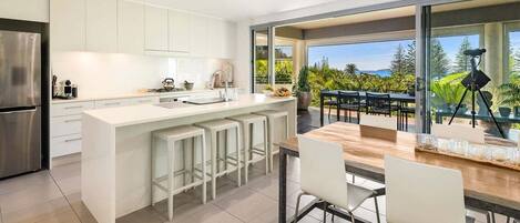 A modern kitchen with a central island, bar stools, and a dining area with a view of the outdoors.