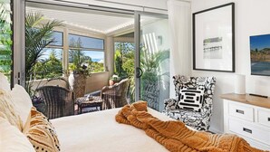 Ein Schlafzimmer mit einem Bett, einem Sessel, einem Schreibtisch und Blick ins Freie.