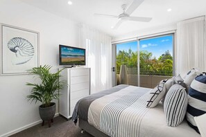 A bedroom with a bed, a television, a ceiling fan, a potted plant, and a balcony with a view of greenery. - Pearl - Resort Pool, Tennis Courts, Beach Front (Sapphire Beach)