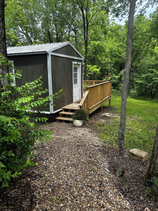 A small shed with a wooden deck and steps leading up to a white door.
